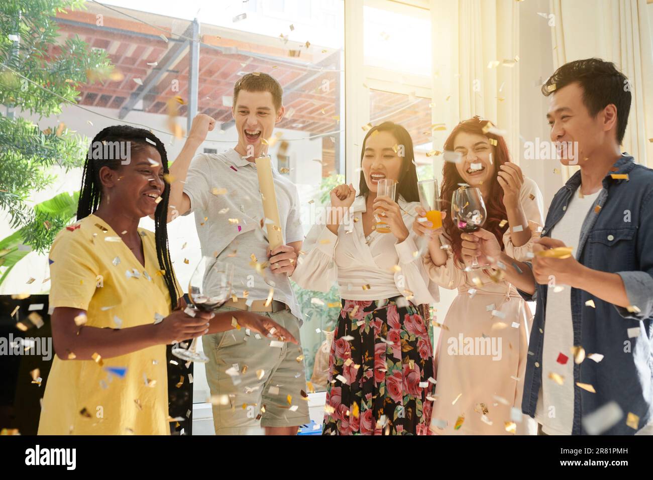 Joyful friends dancing and drinking under falling confetti Stock Photo