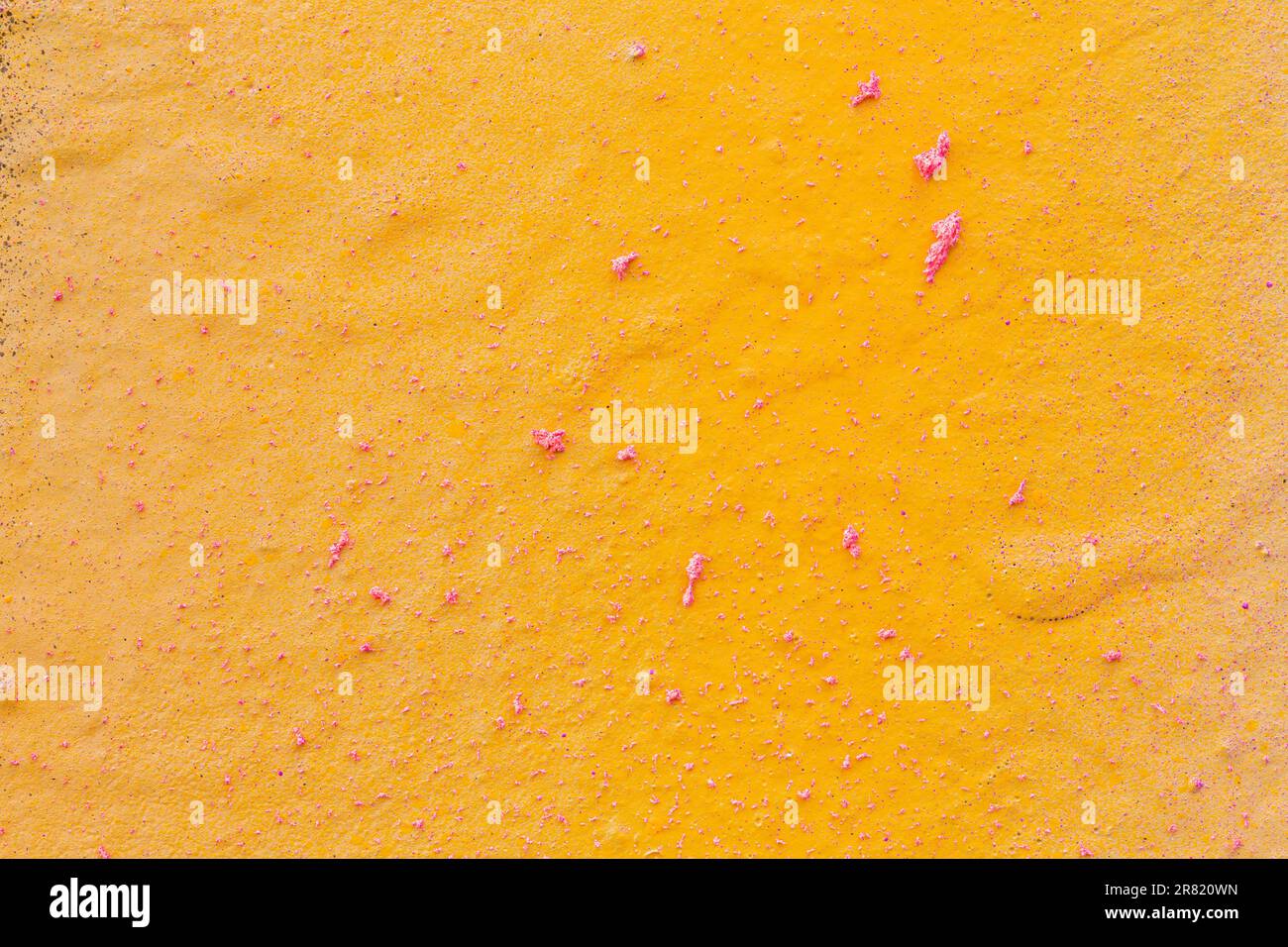 Close-up of a spray painted yellow orange wall with pink splashes. Abstract full frame textured grunge graffiti background with copy space. Stock Photo