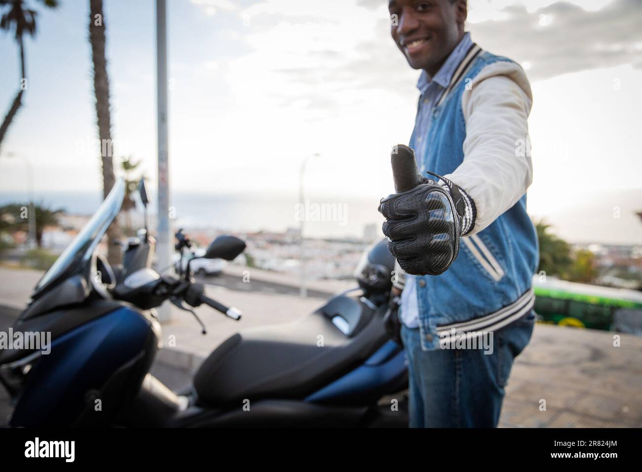 A happy biker shows thumbs up while standing by his scooter, road ...