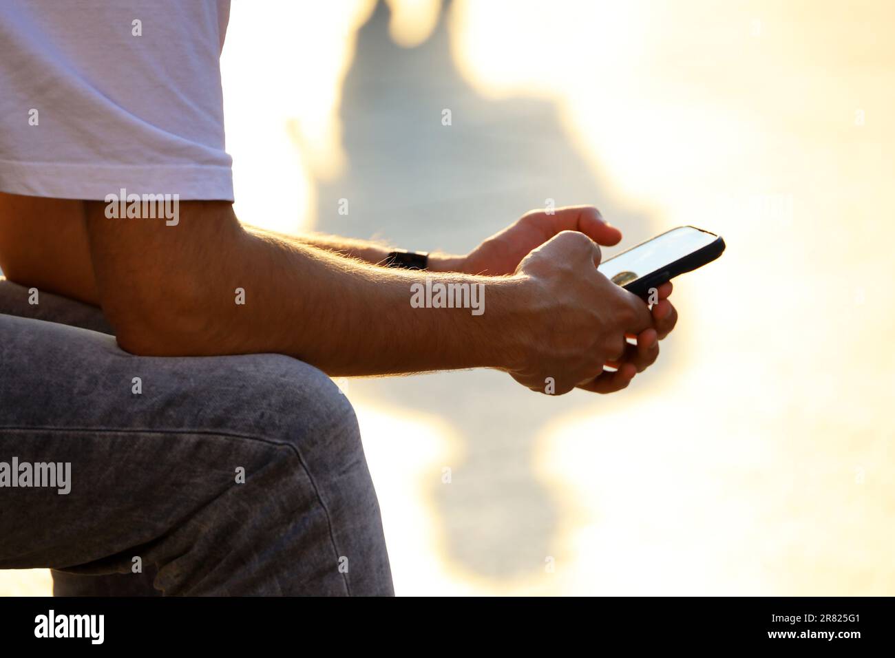Smartphone in hands of man sitting on a street in sunlight. Using phone