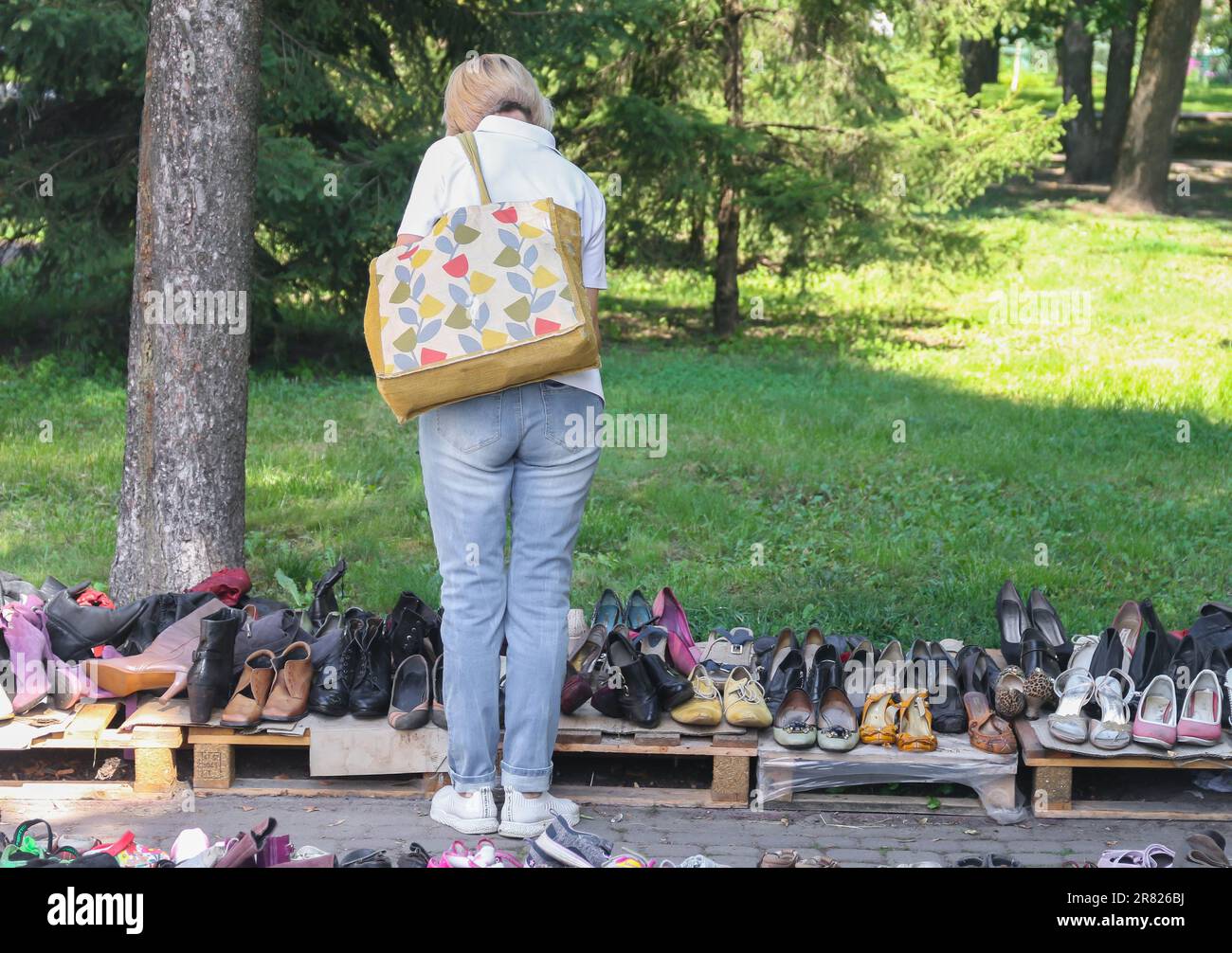 A person in casual wear standing next to a pile of used shoes in an outdoor market setting Stock