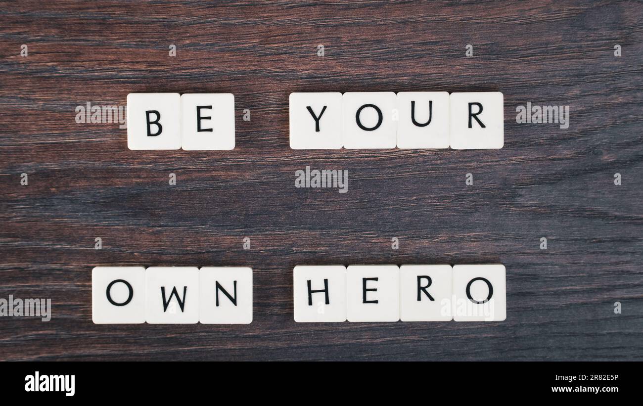 Be your own hero word on white stones. Motivational quote concept. Motivational words on little white stones on wooden table. High angle view. Stock Photo