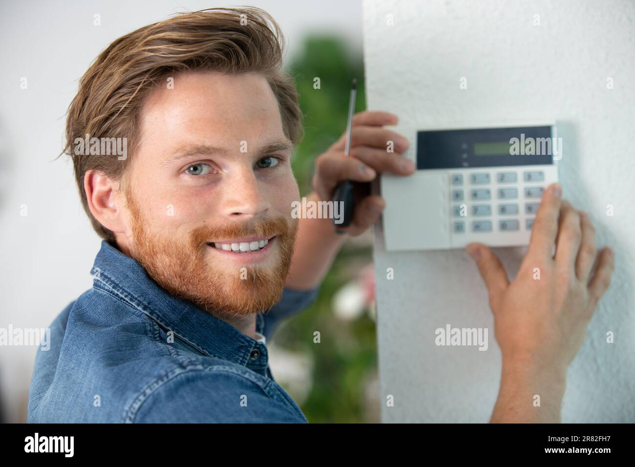 male electrician installing security system door sensor on wall Stock