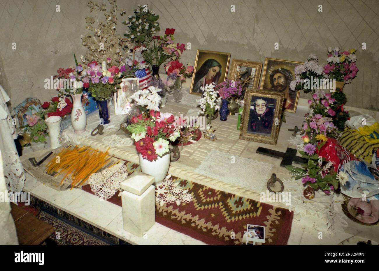 Romania, approx. 2000. A stone burial vault topped with religious icons, flowers and candles. Stock Photo