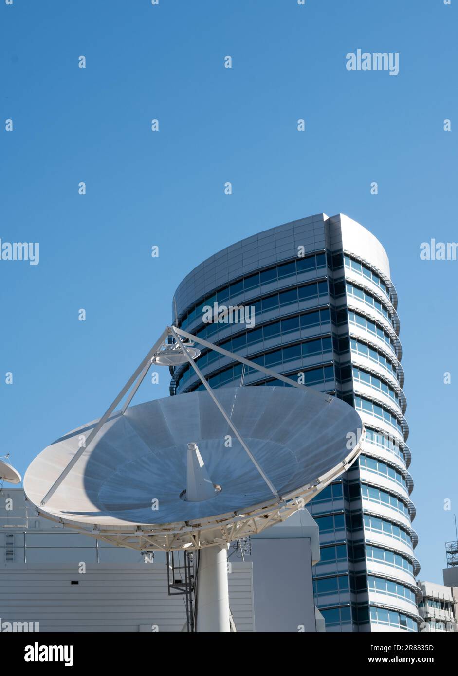 A satellite receiver dish sits atop a smaller building in the foreground. The high-rise building in the background offers a confusing sense of scale i Stock Photo