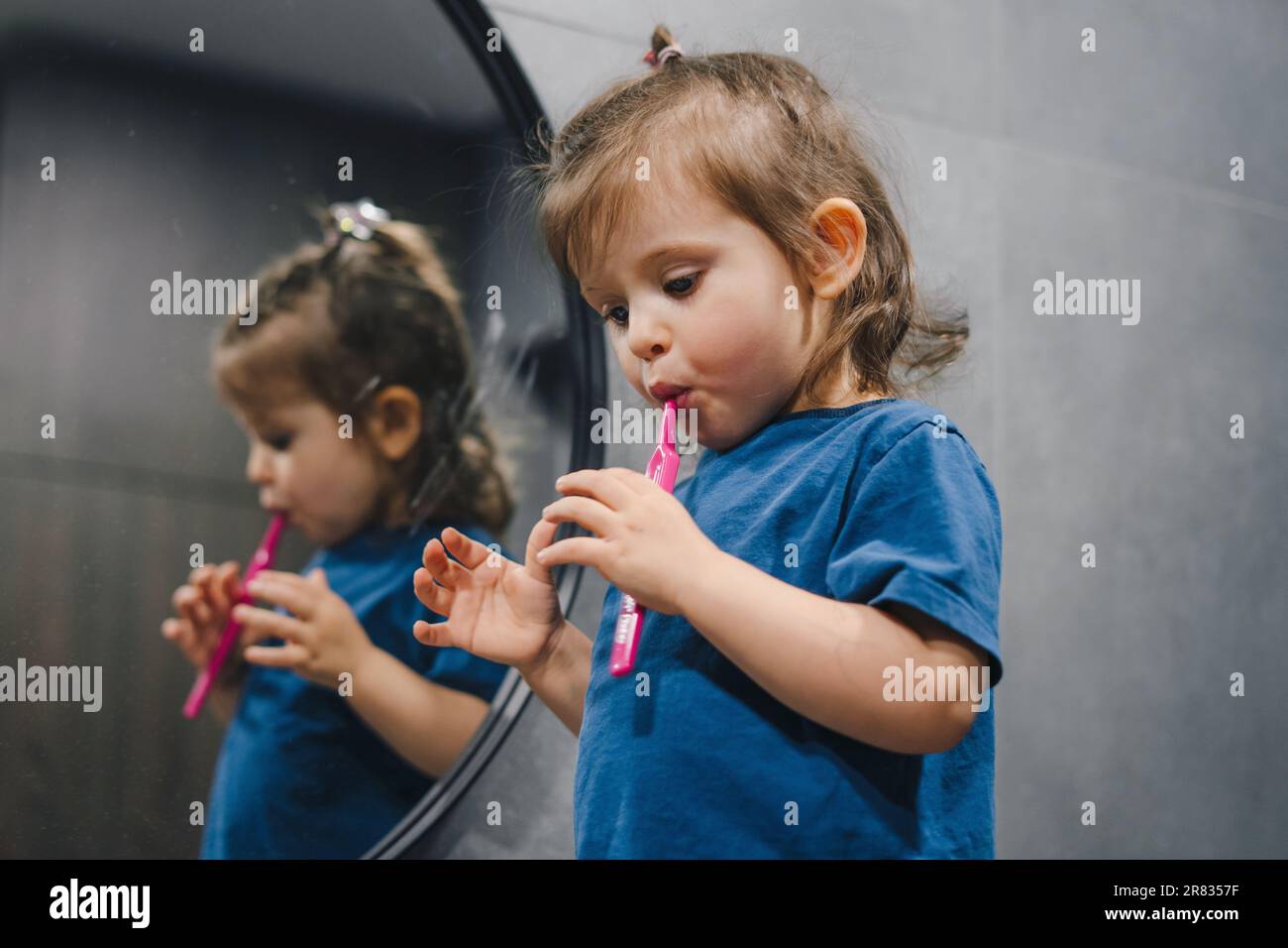Adorable child learning how to brush her teeth in the bathroom