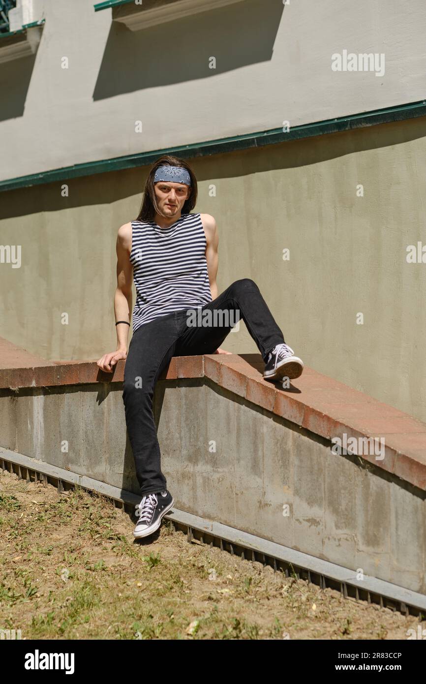 Creative long-haired man in tank top and jeans sits on railing Stock ...