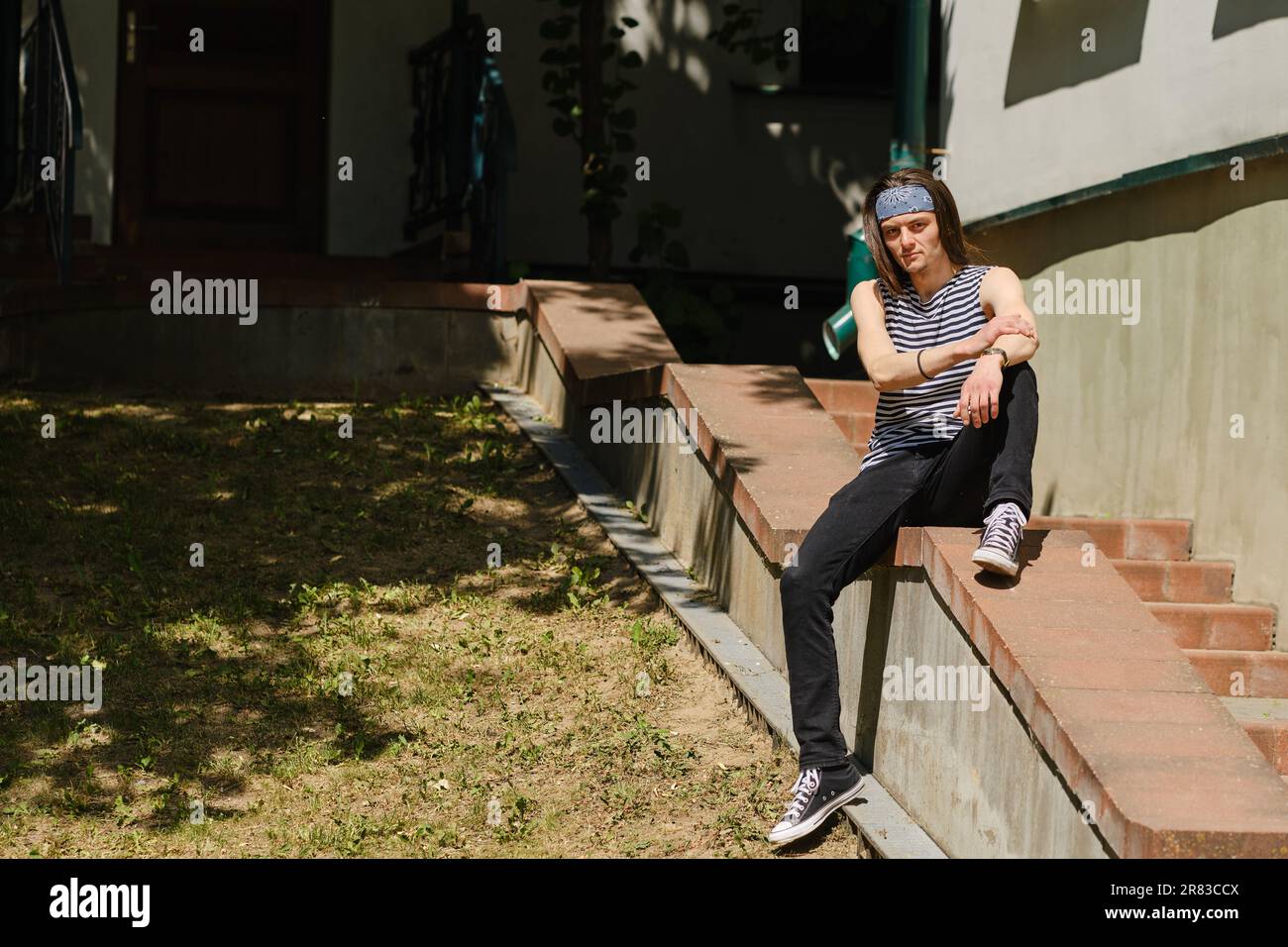 Creative long-haired man in tank top and jeans sits on railing Stock ...