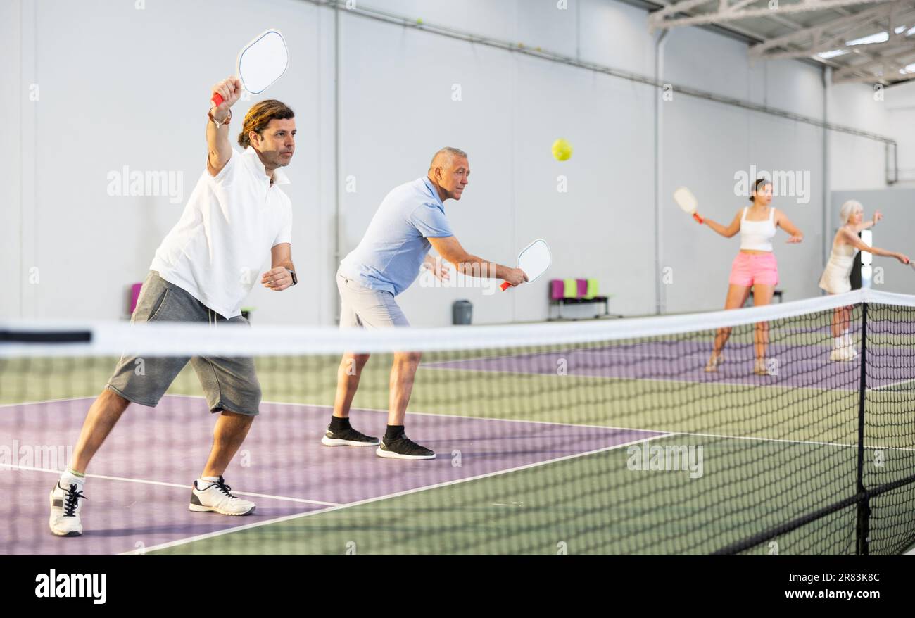 Adult man playing doubles pickleball with aged partner indoors Stock