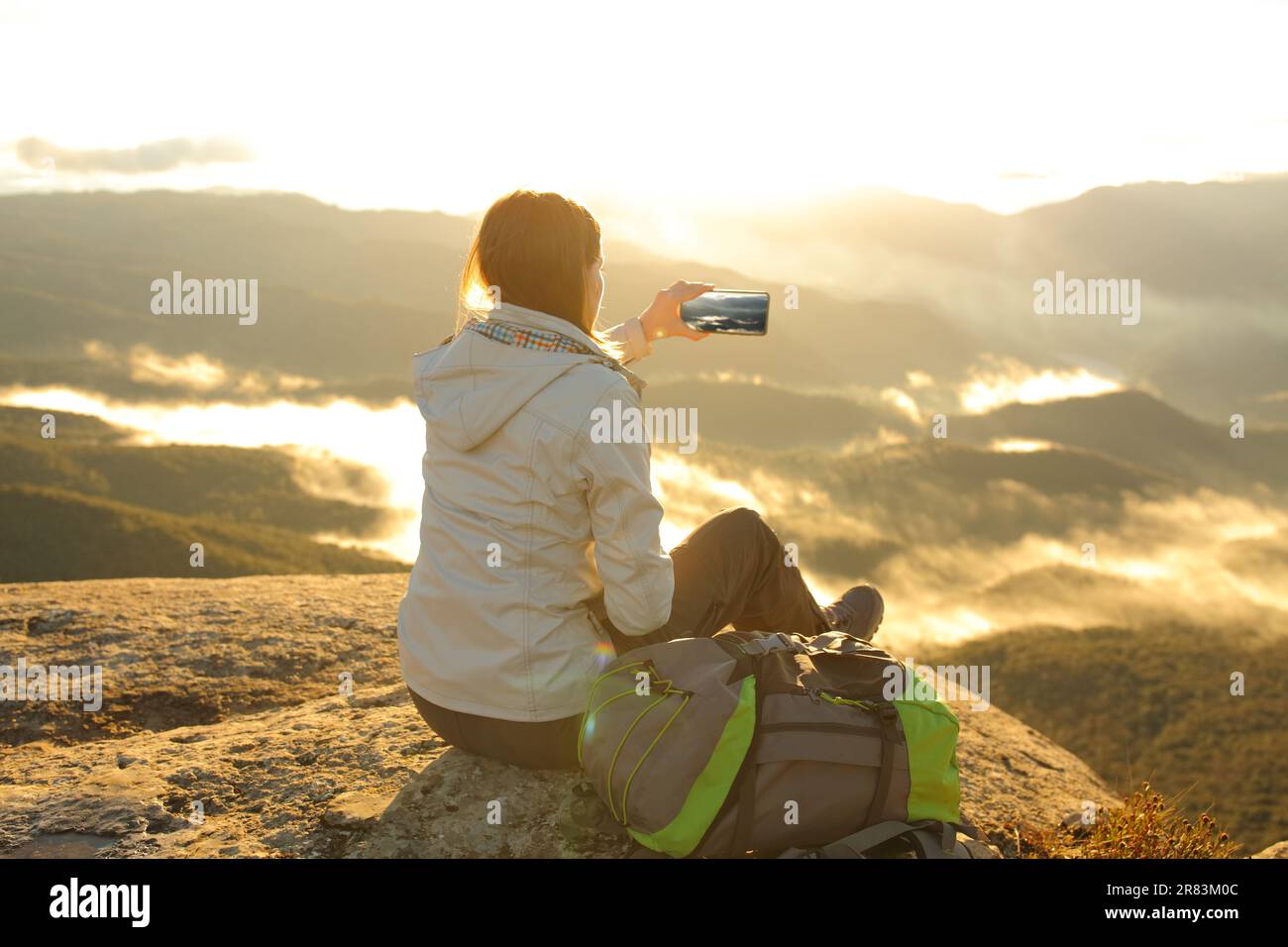 Single trekker taking photo of a mountain on smartphone at sunrise Stock Photo