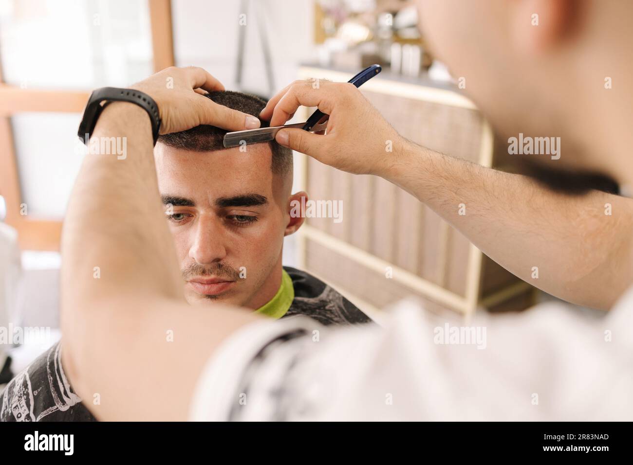 Barber using razor to shave beard for customer. Confident guy sitting