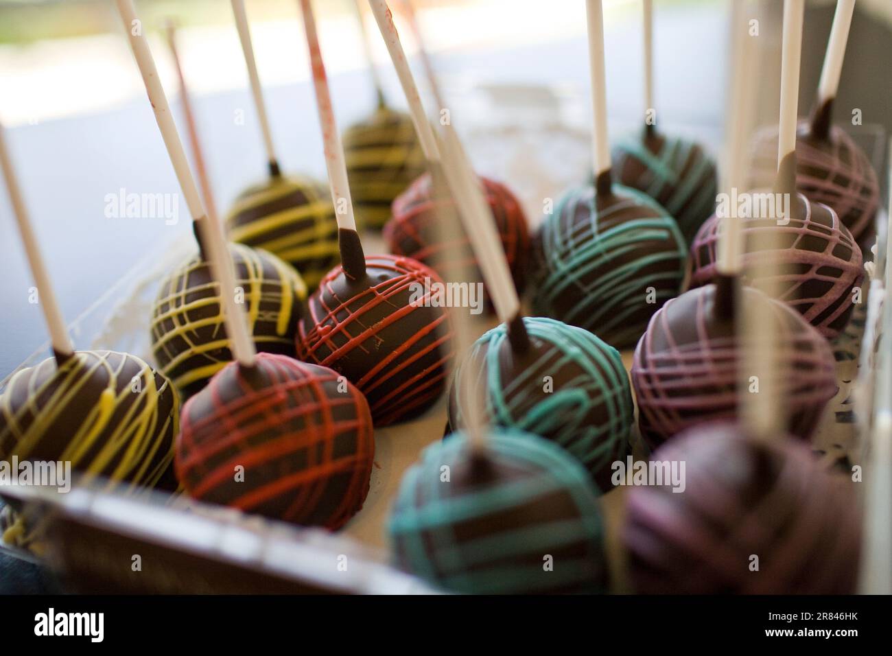 Close up, selective focus view of colorfully drizzled chocolate candy balls on sticks. Stock Photo