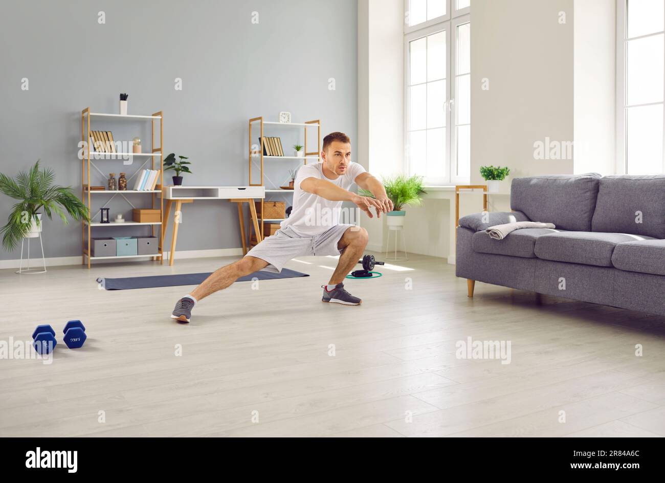 Fit young man doing side lunge stretching exercises during sports workout at home Stock Photo