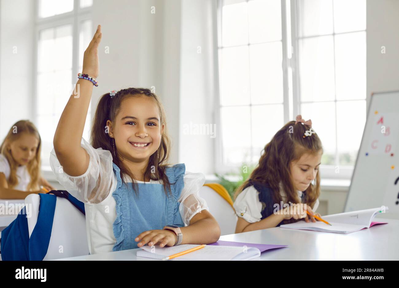 Girl elementary school student rising hand sitting at desk on lesson in ...