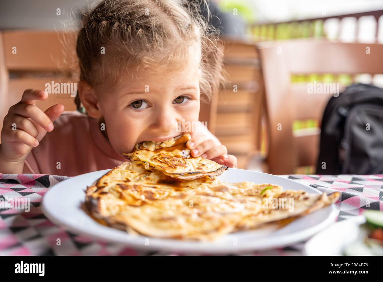 Little girl eating potato and cheese gozleme on wooden table