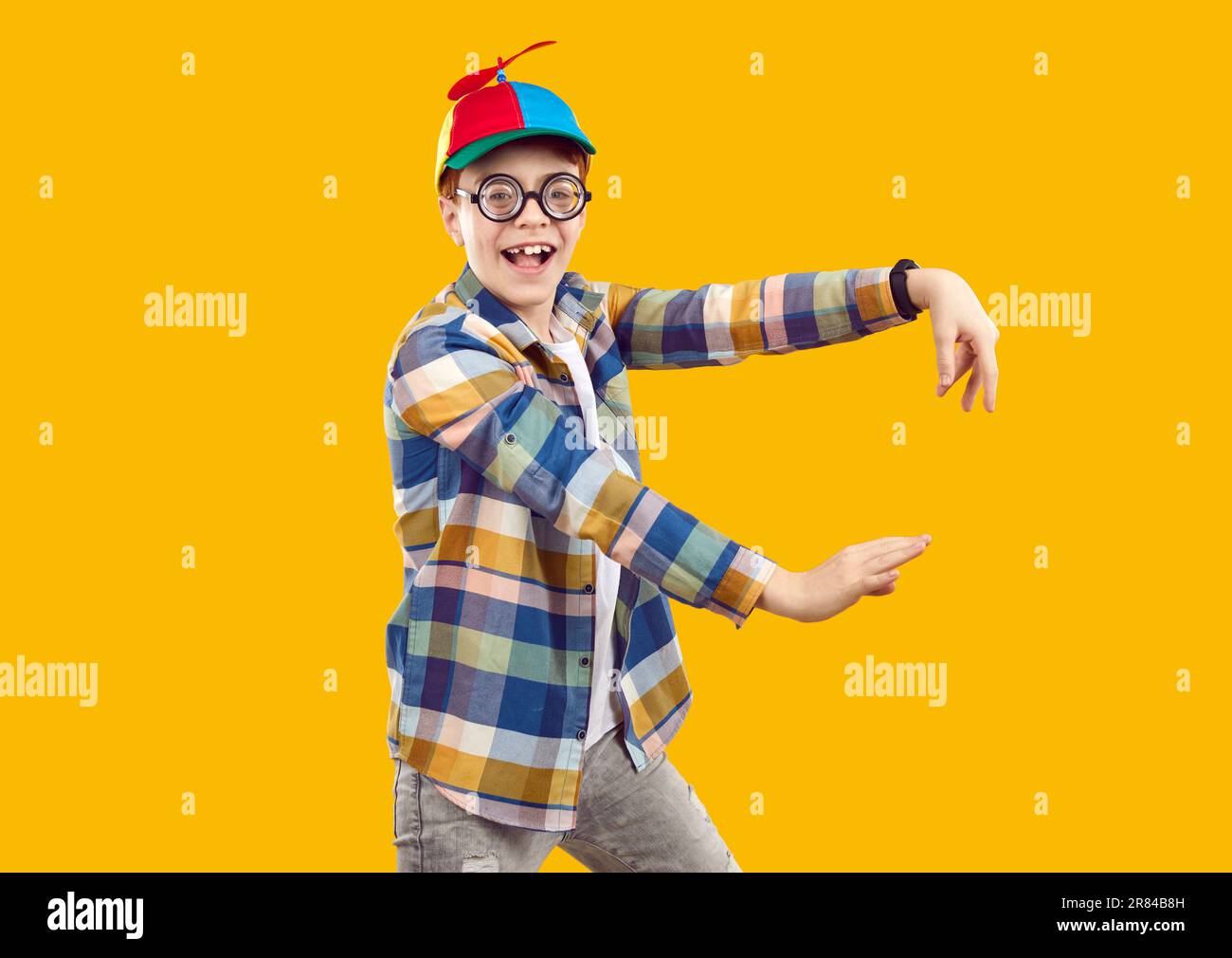 Happy funny child in shirt, propeller cap and glasses dancing on orange