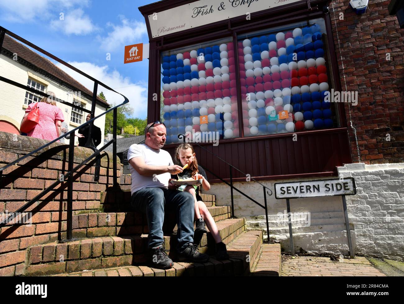 Man and child eating fish and chips outside chip shop decorated for the coronation of King Charles III. Picture by DAVID BAGNALL Stock Photo
