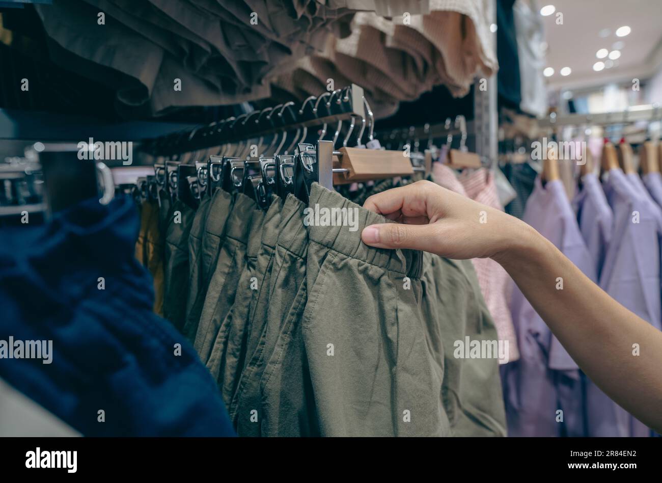Woman shopping green shorts in clothing store. Woman choosing clothes. Shorts on hanger hanging on rack in clothing store. Fashion retail shop inside Stock Photo