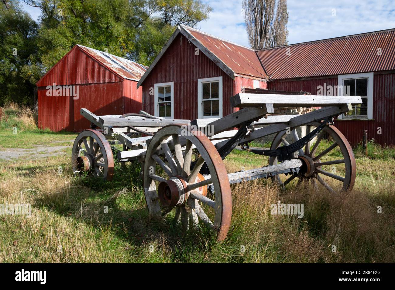 Derelict wooden wagon in front of red barn, St James Station near Hanmer Springs, Canterbury, South Island, New Zealand Stock Photo