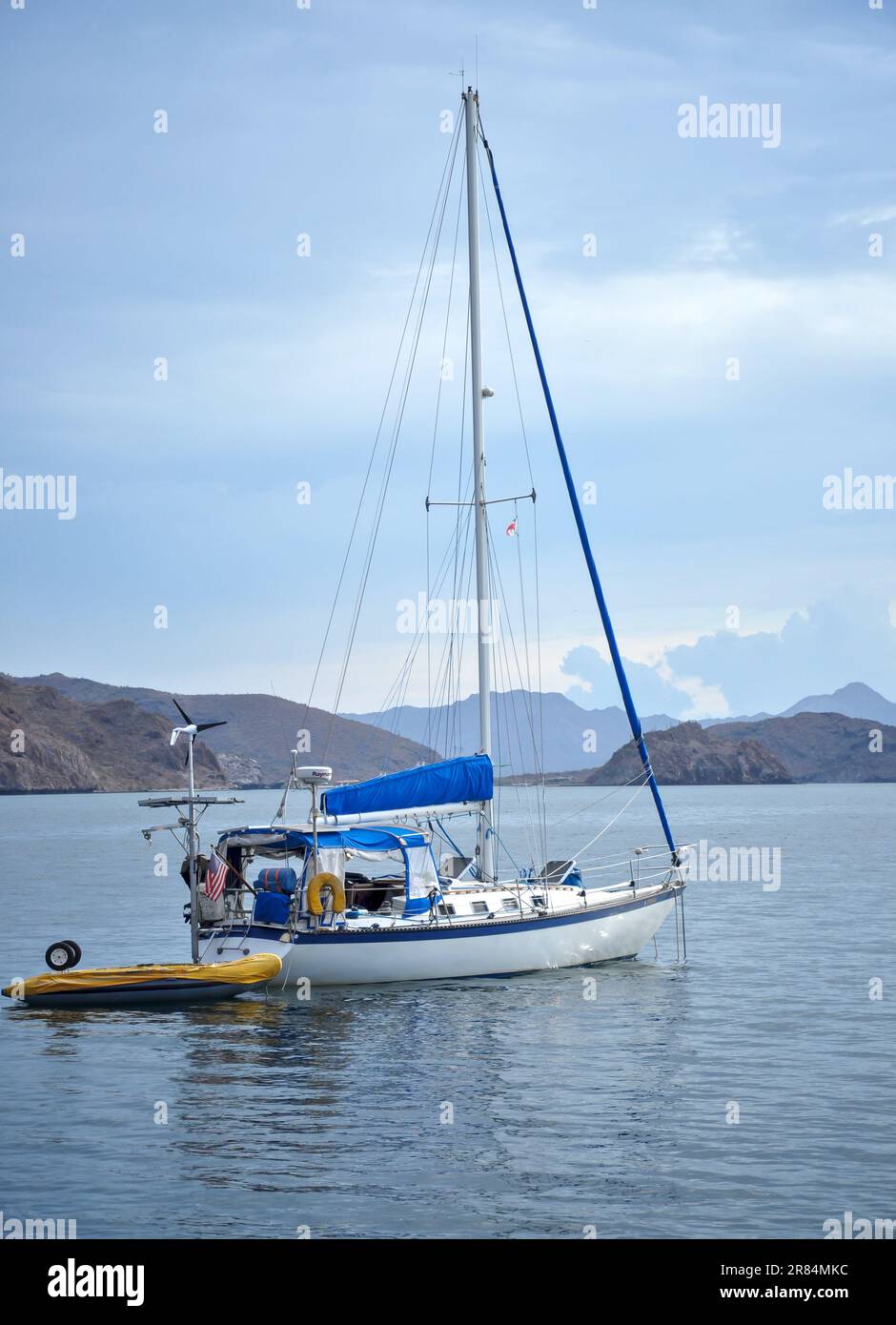 A cruising sailboat, its dinghy with tied aft, at anchor in calm seas