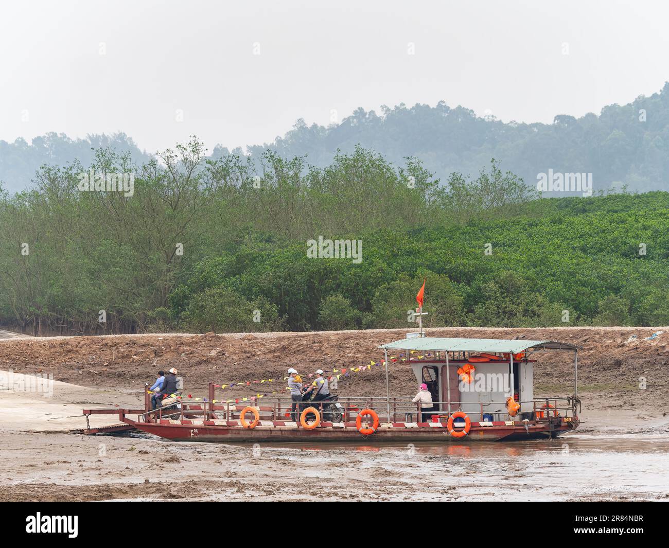 Simple car ferry arriving after crossing a river in Thanh Hoa Province in Vietnam with passengers and a couple of motorbikes disembarking. Stock Photo
