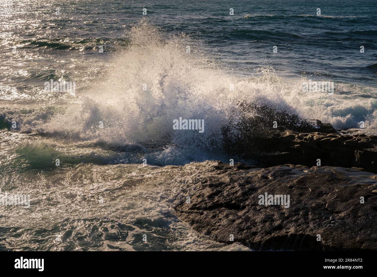 A large wave crashes into a rocky shoreline Stock Photo