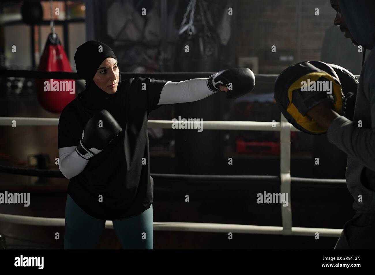 Young Muslim female boxer hitting boxing pads on hands of her trainer