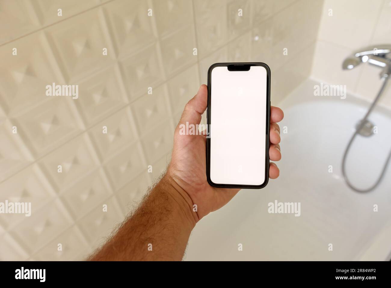 Smartphone mockup in bathroom, man holding mobile phone with blank touch screen over the bathtub, selective focus Stock Photo