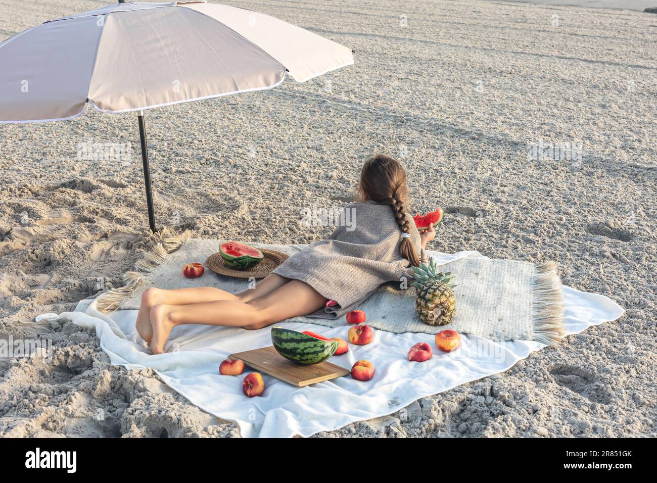 Little girl eats fruit lying on a blanket on the beach Stock Photo Alamy