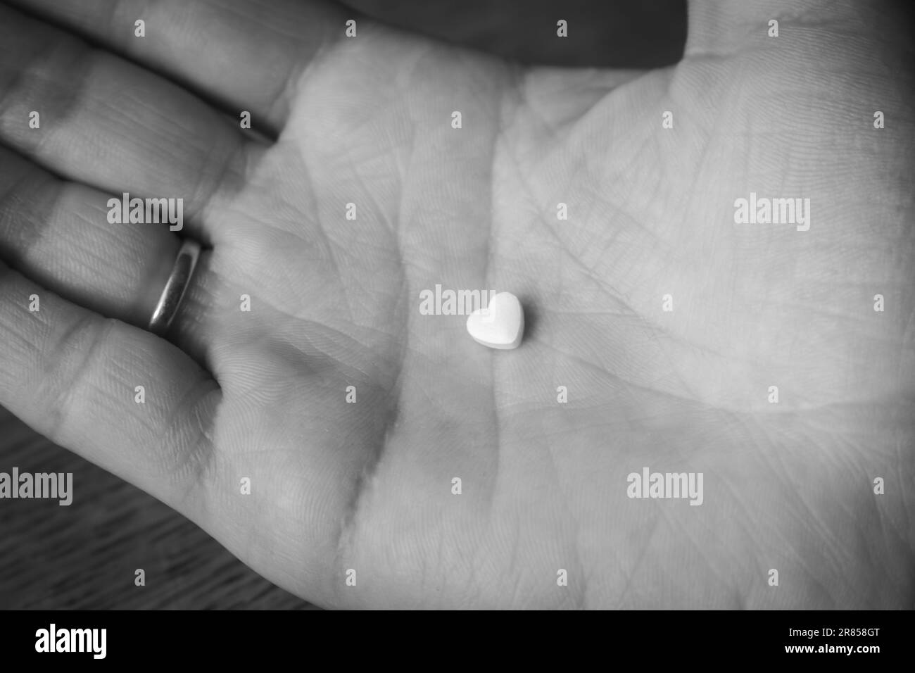 White pill on open palm hand, monochrome. Heart shape pill in hand, black and white. Medical treatment. Painkiller from unhappy love. Stock Photo