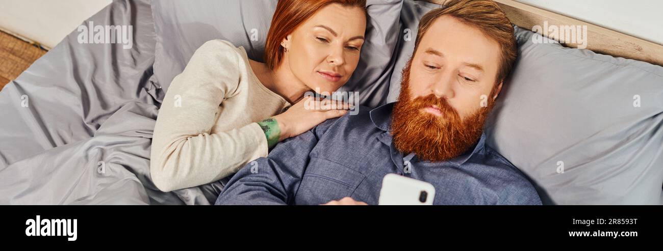 top view, networking, relaxation time, tattooed couple relaxing, weekends without kids, husband and wife, bearded man using smartphone near redhead wo Stock Photo