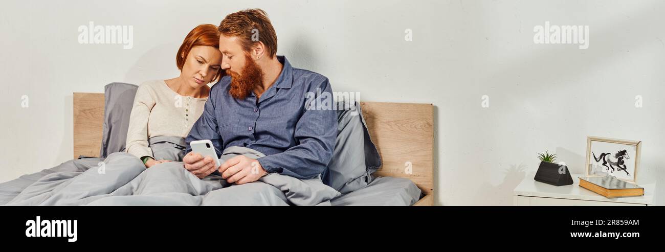digital couple, screen time, networking, relaxing on weekends without kids, sad husband and wife, bearded man and redhead woman using smartphone, day Stock Photo
