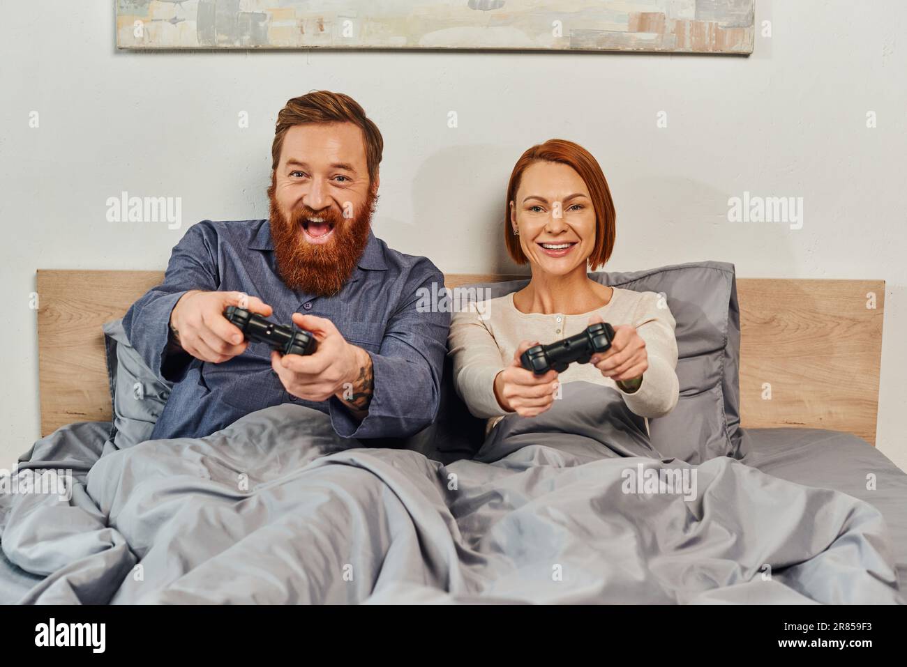 weekends without kids, redhead husband and wife playing video game, bearded man and happy woman holding joysticks, excited, gaming fun, married couple Stock Photo