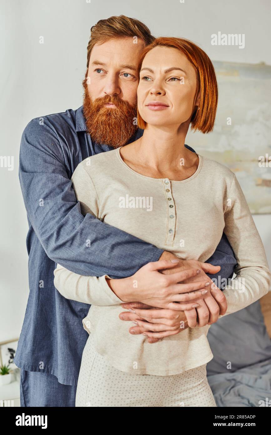 married couple hugging in cozy bedroom, day off without kids, redhead husband and wife, enjoying time together, weekends together, tattooed, bonding, Stock Photo