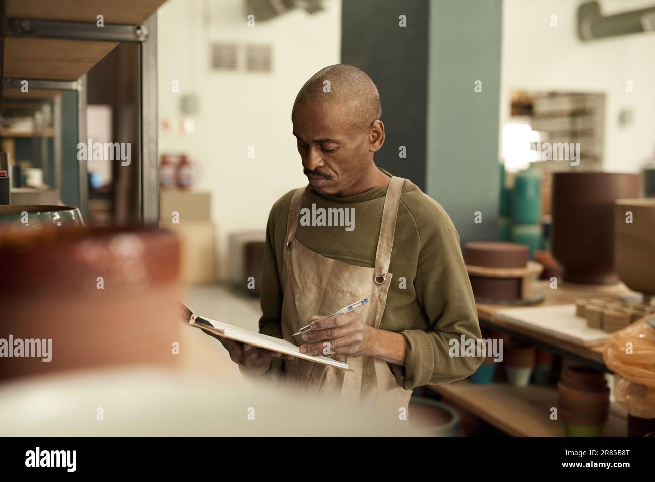 African potter taking inventory of pots on shelves in a ceramics workshop Stock Photo