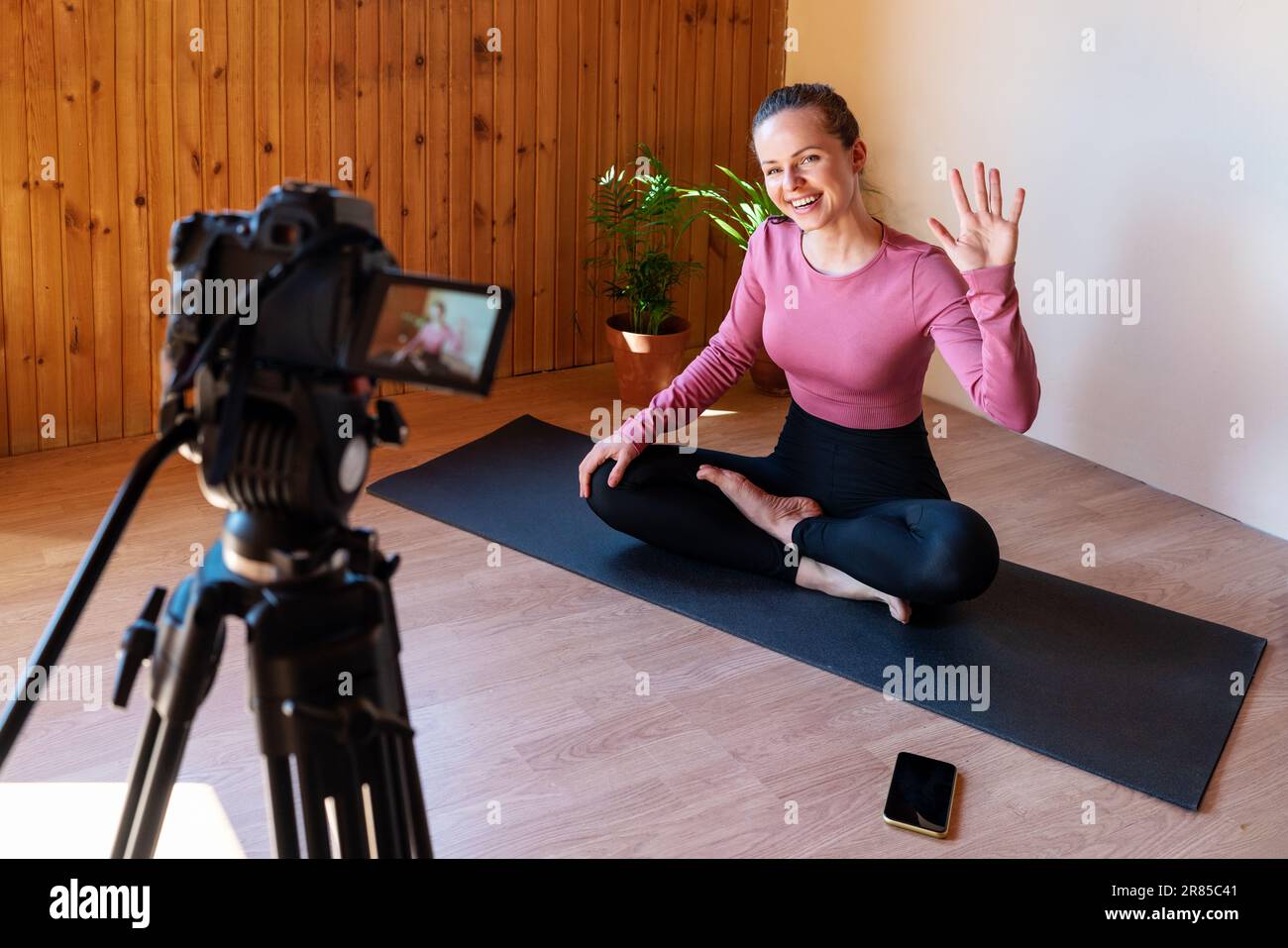 Woman fitness coach video blogger waving hand welcoming subscribers while recording her sport training. Stock Photo