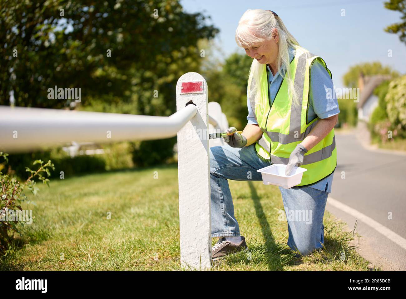 Senior Retired Woman Helping To Maintain Community By Painting Fence Post Stock Photo