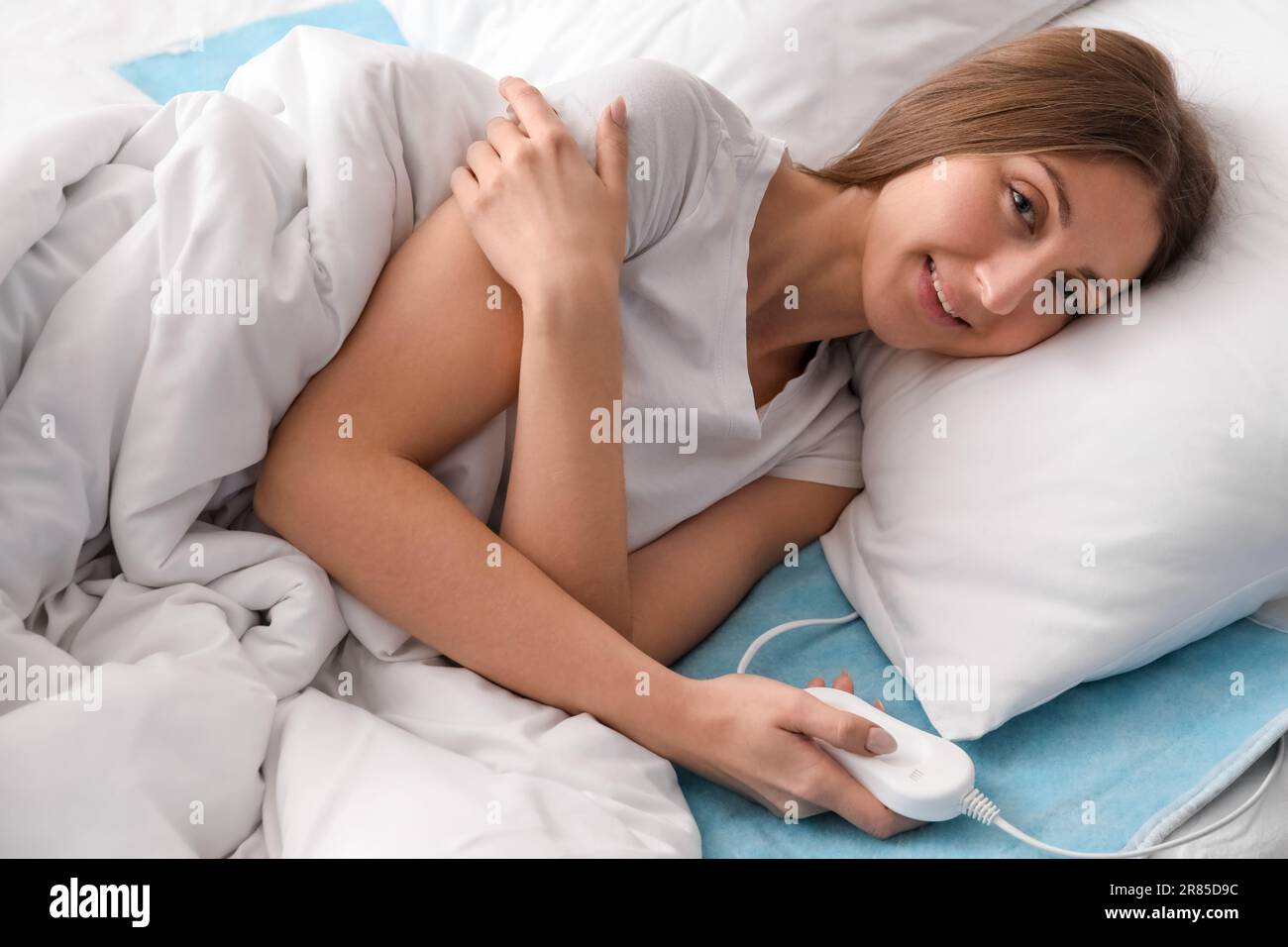 Young woman lying on electric heating pad in bedroom Stock Photo Alamy