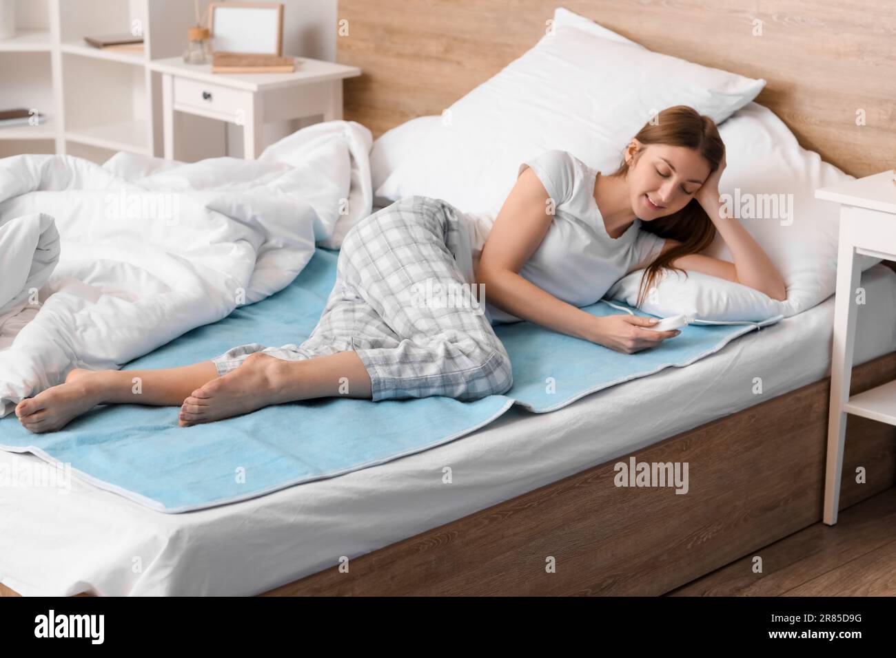 Young woman lying on electric heating pad in bedroom Stock Photo Alamy