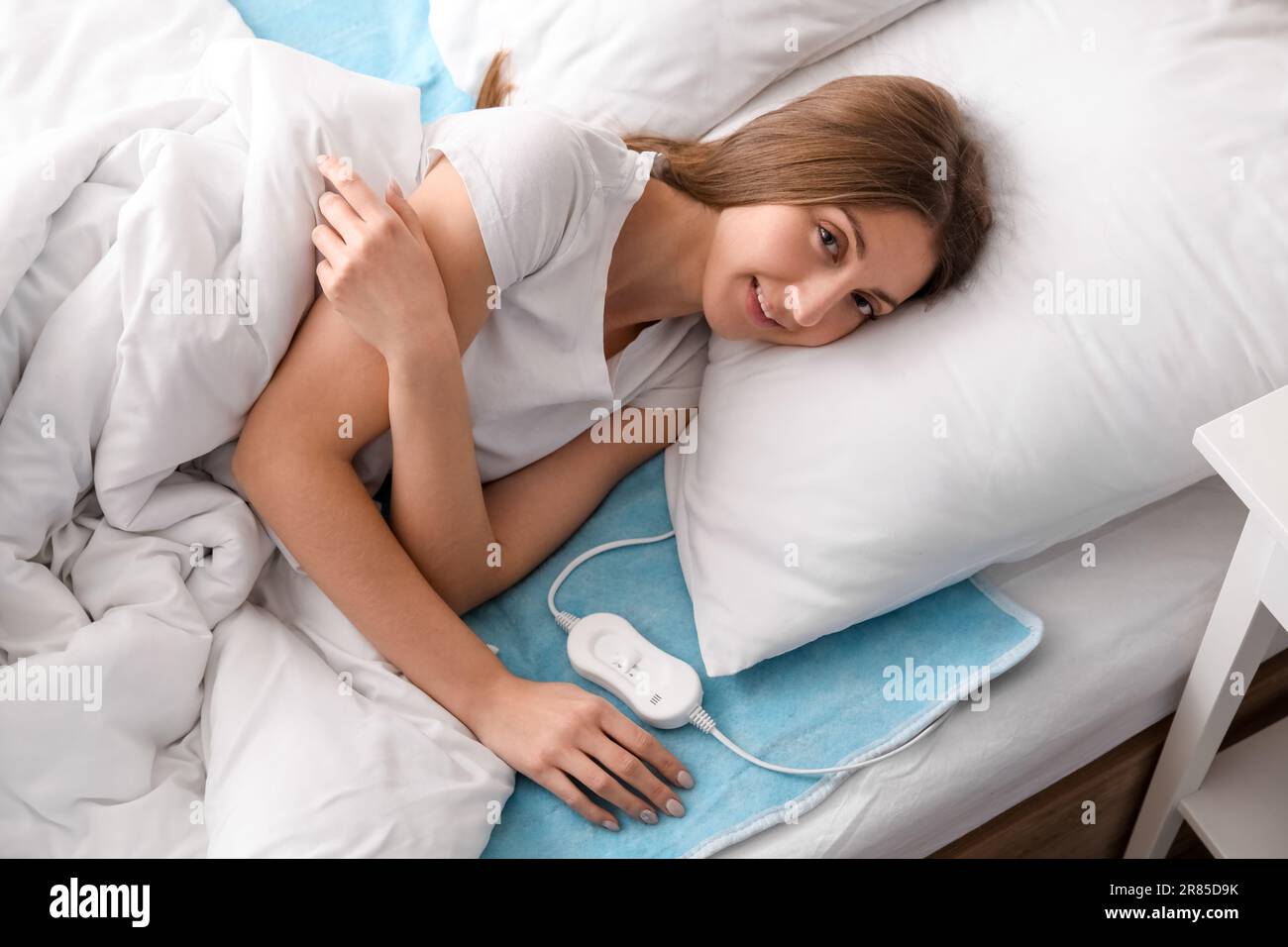 Young woman lying on electric heating pad in bedroom Stock Photo Alamy
