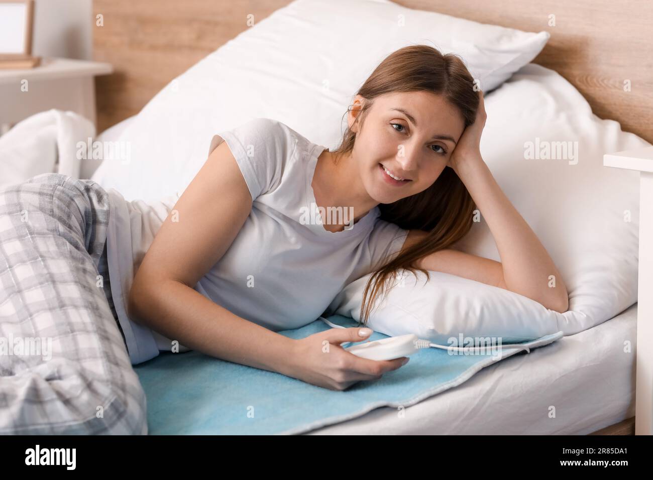 Young woman lying on electric heating pad in bedroom Stock Photo Alamy