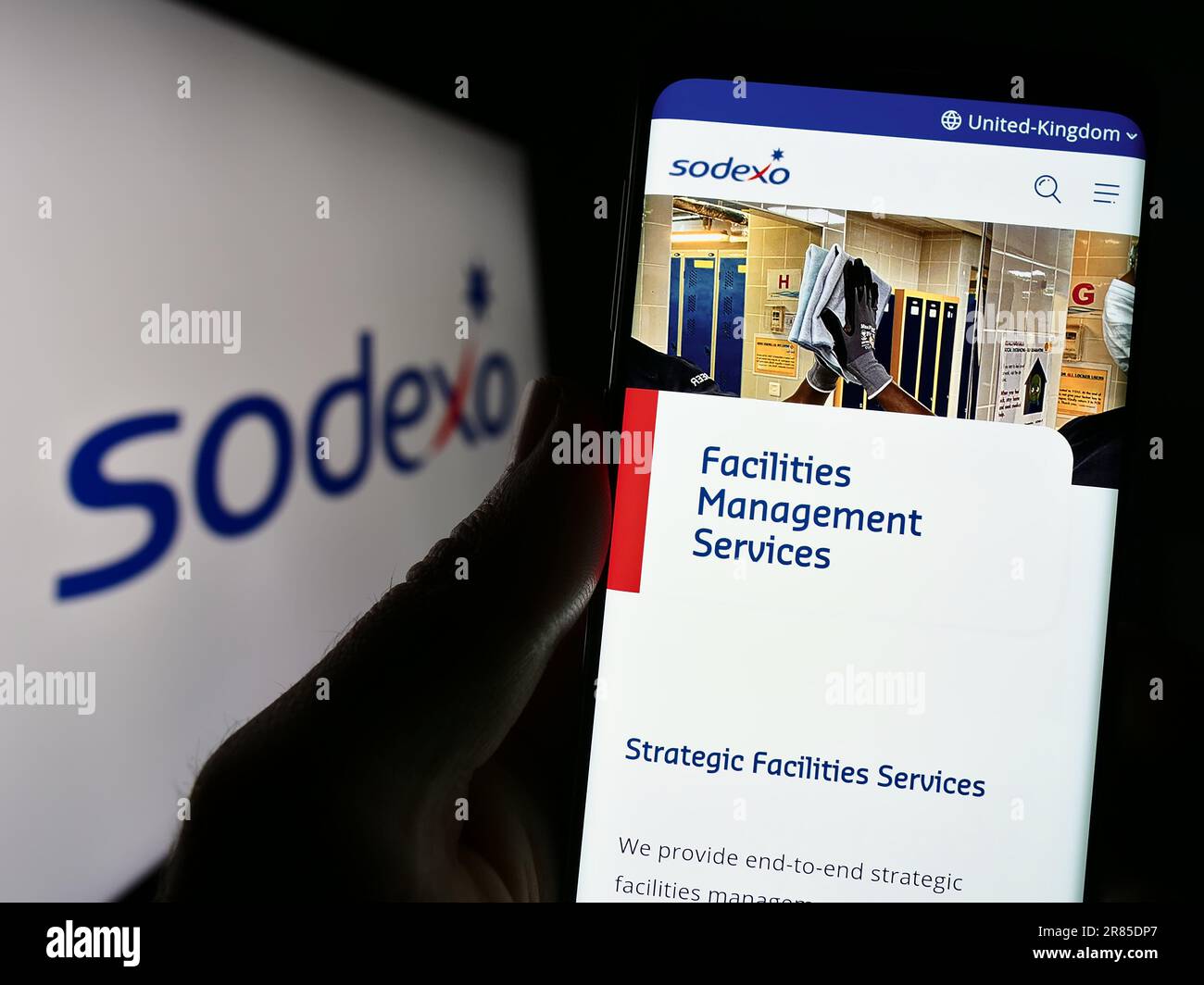 Person holding smartphone with webpage of French facility management company Sodexo S.A. on screen with logo. Focus on center of phone display. Stock Photo