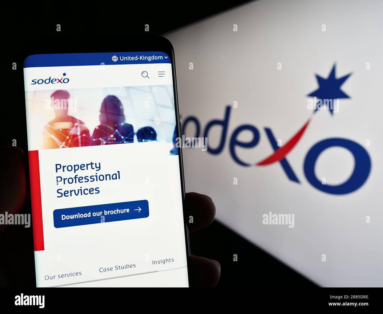 Person holding cellphone with web page of French facility management company Sodexo S.A. on screen with logo. Focus on center of phone display. Stock Photo