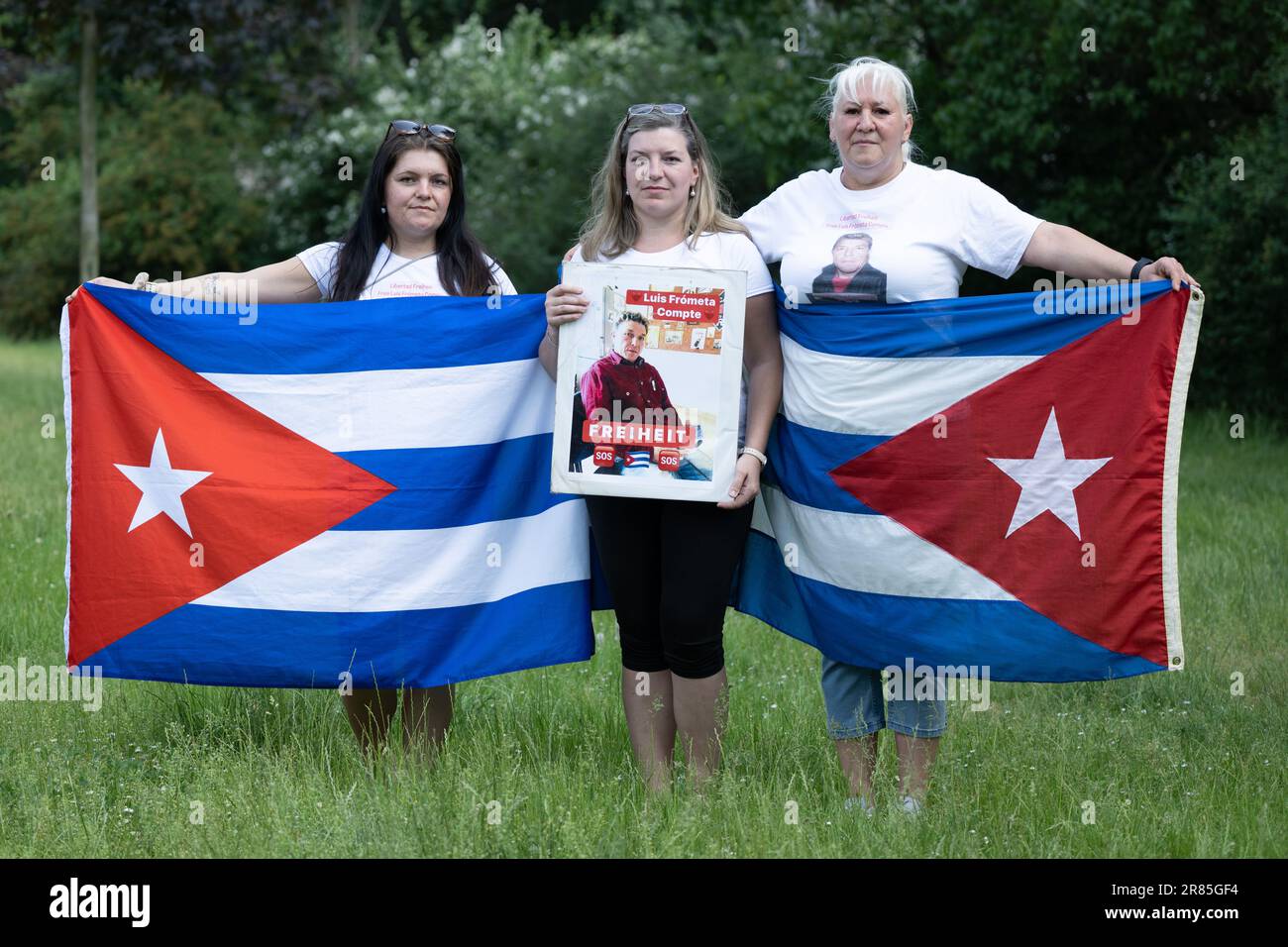 PRODUCTION - 12 June 2023, Saxony, Dresden: Maria (l-r) and Janie Frometa Compte, daughters of imprisoned German-Cuban Luis Frometa Compte, and Silke Frometa Compte, wife, stand on the sidelines of a rally in Alaunpark holding a photo of Luis Frometa Compte. Frómeta Compte, from Dresden, had been on a family visit to Havana in July 2021, when demonstrations for freedom and against mismanagement erupted in many cities of the socialist Caribbean nation. Frómeta Compte was arrested for filming one of the protests with a cell phone, according to his family. He was convicted of sedition, and an ori Stock Photo