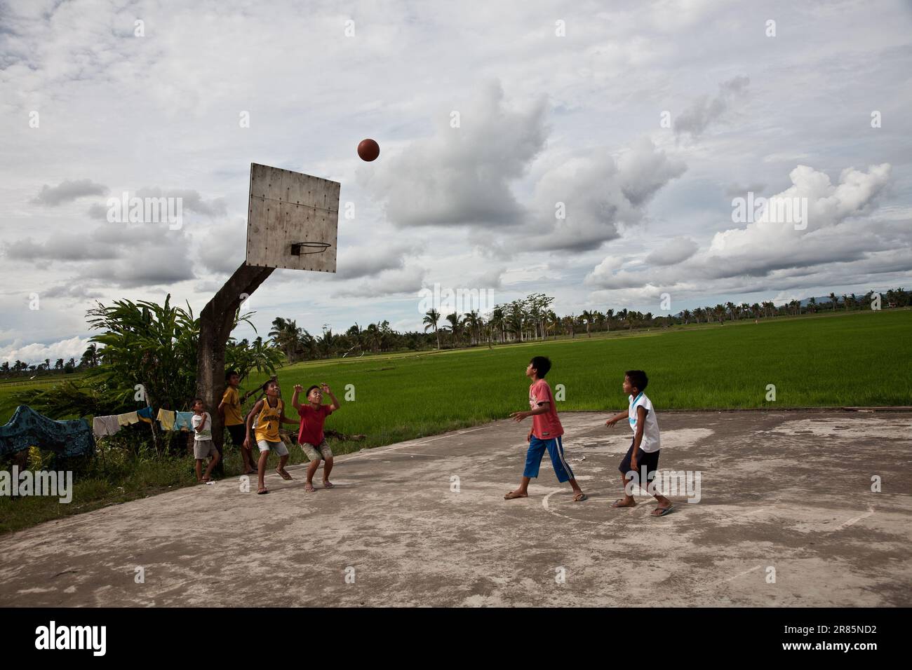 Children playing basketball in a court by a rice field in Mindanao, Philippines. Philippines is a co-host of the 2023 FIBA Basketball World Cup. Stock Photo