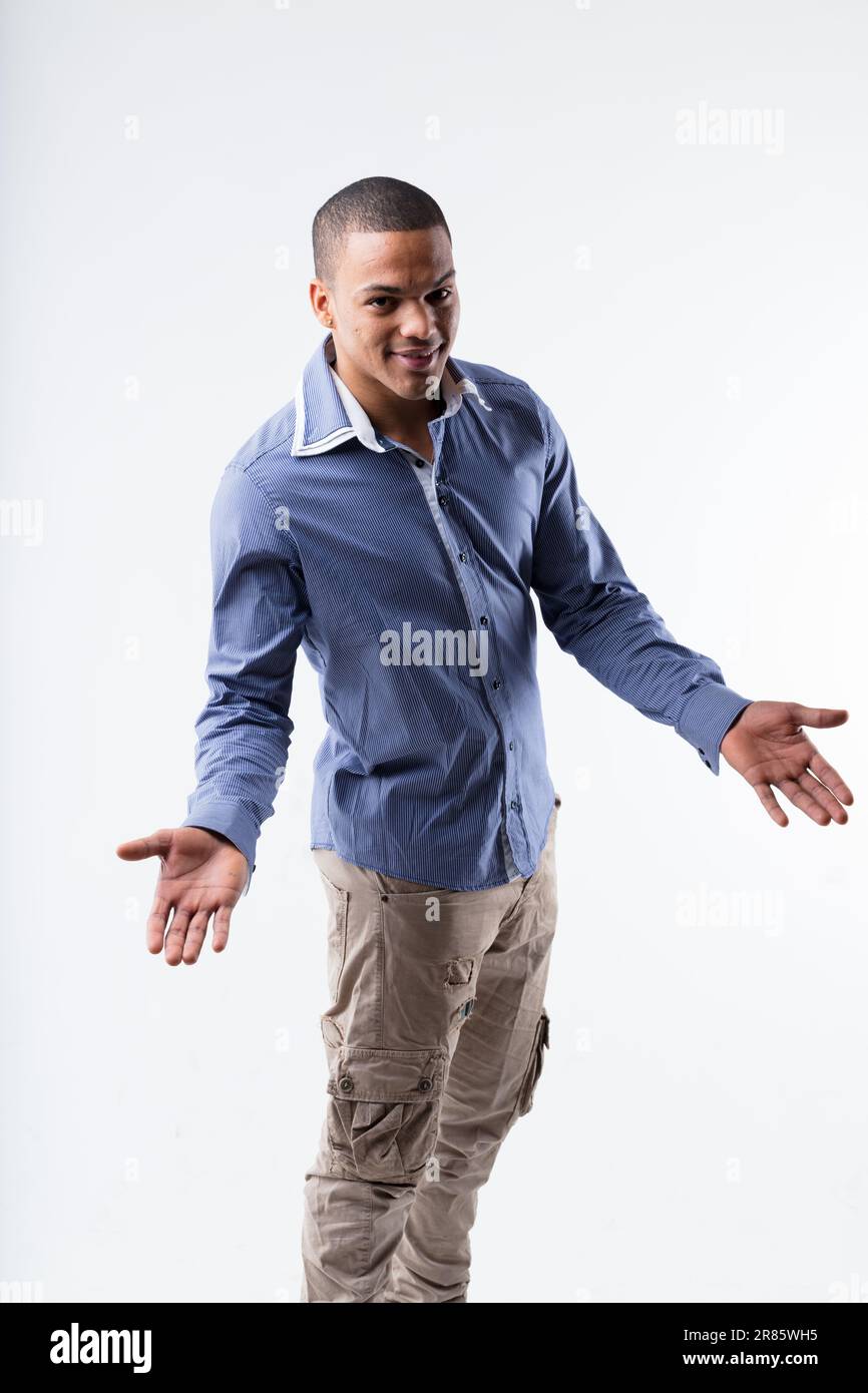 Cool! Young black man greets joyfully with open arms. Wears blue shirt and light trousers, expressing joy and openness. Smiles in a high-angle shot on Stock Photo