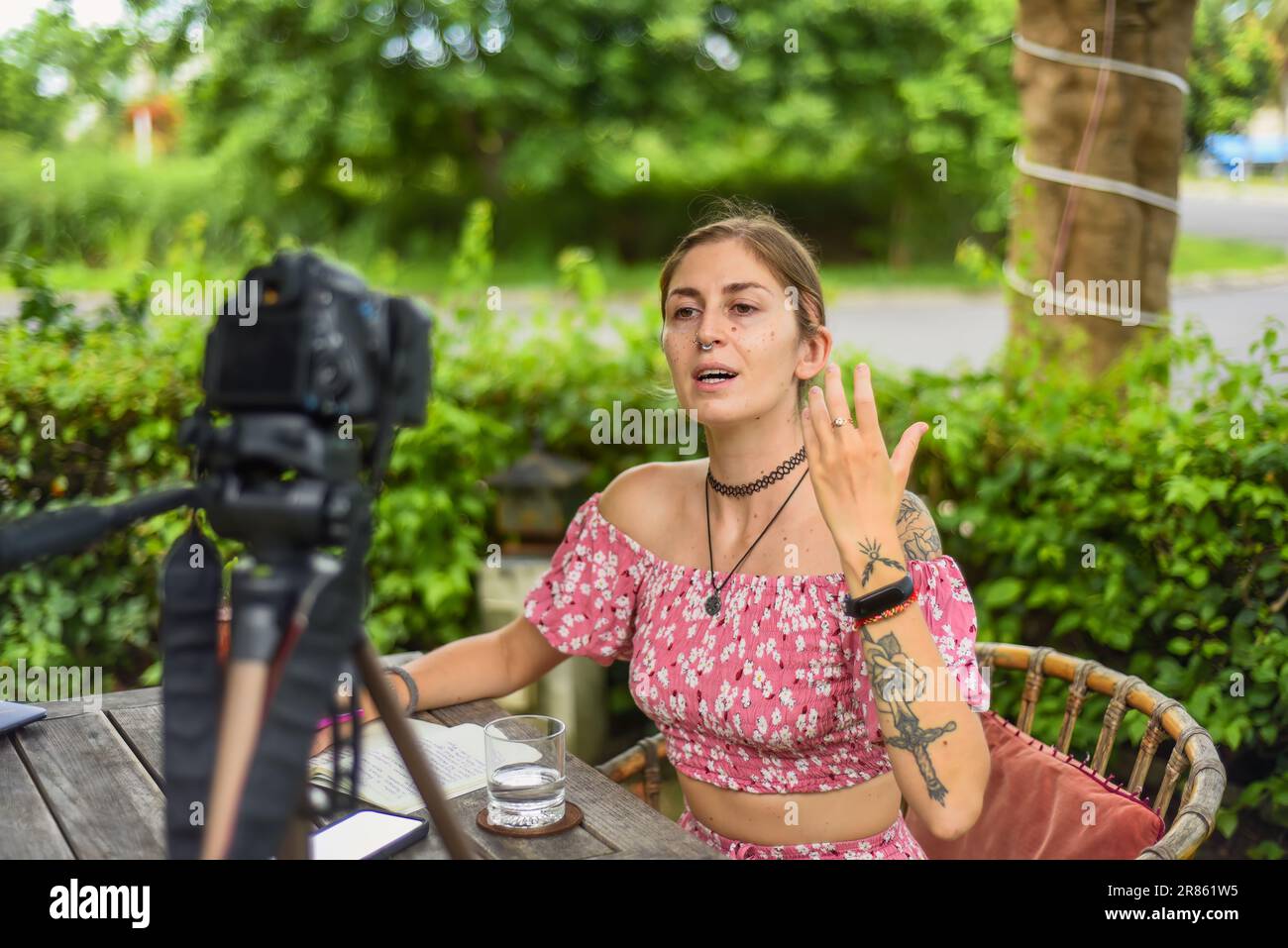 Cute videographer and vlogger taking a video with camera and tripod in summer garden Stock Photo