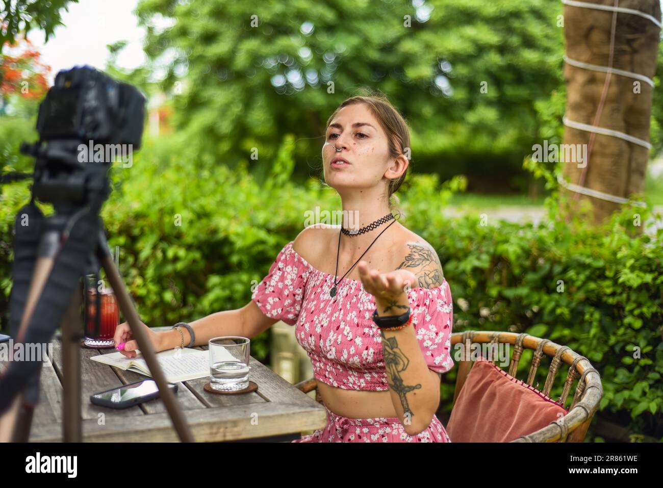Cute videographer and vlogger taking a video with camera and tripod in summer garden Stock Photo