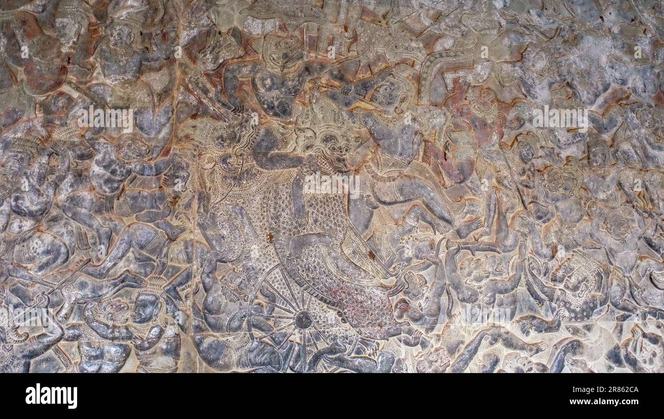 Stone wall with intricate carvings of battle scenes from Hindu mythology, found in an ancient Khmer temple, showing the depth of ancient art. Stock Photo