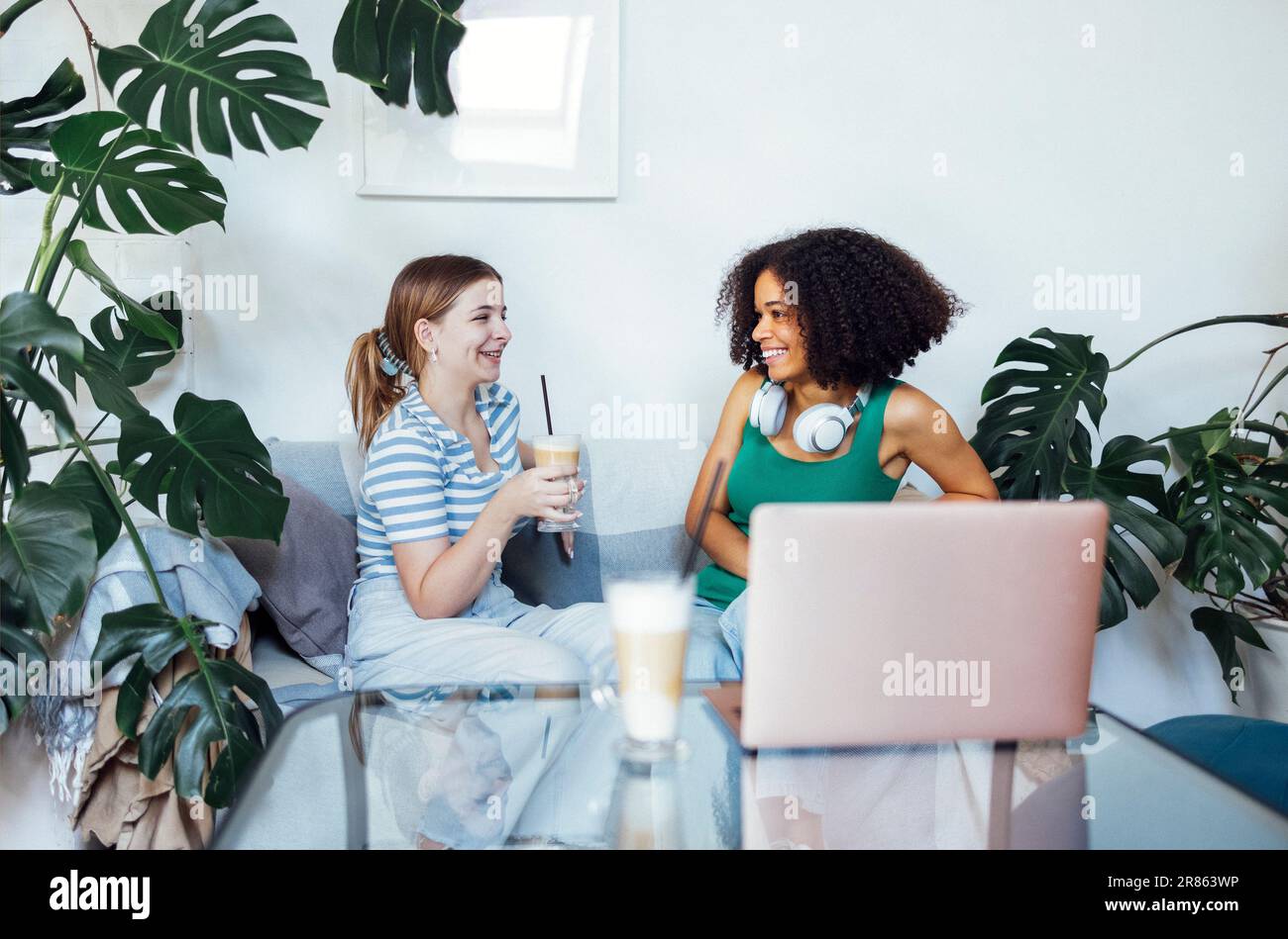Attractive multiracial teenagers drink cappuccino and chat. Funny teen girls talk and have good time together. Smiling female friends having fun at ho Stock Photo